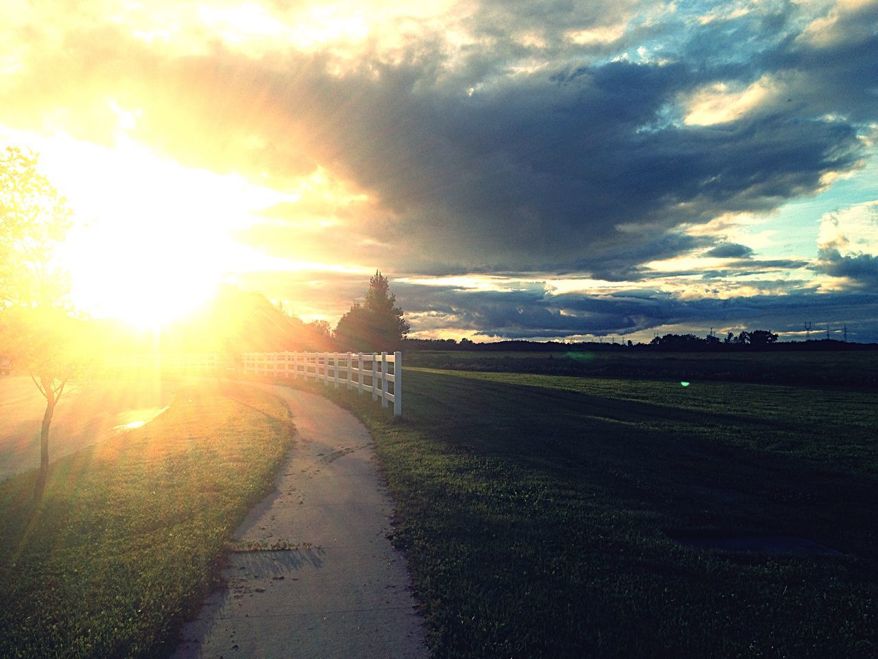 sunset, landscape, sun, the way forward, road, long, tranquility, sky, tranquil scene, cloud - sky, cloudy, cloud, footpath, day, nature, outdoors, sunbeam, scenics, diminishing perspective, solitude, empty road, park, country road, surface level, narrow, beauty in nature, dramatic sky, lens flare, storm cloud