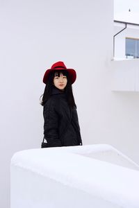 Portrait of young woman standing against white wall