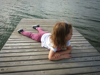 High angle view of girl sitting on pier over lake