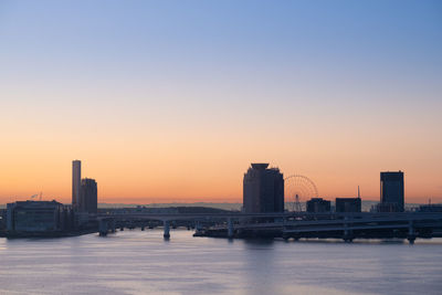 Sea by buildings against clear sky during sunset