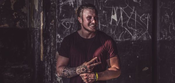 Handsome man with tattoo showing peace sign while standing against wall