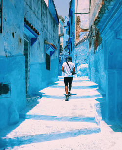 Rear view of man walking on alley amidst buildings in city