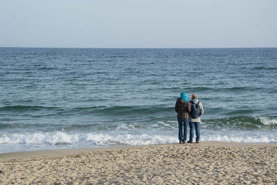 Rear view of man standing at beach against clear sky