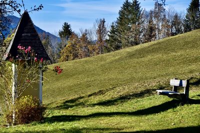 Scenic view of field with bench and chapel by trees against sky