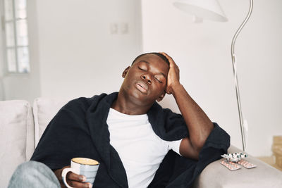 Tired man holding coffee cup while sitting on sofa