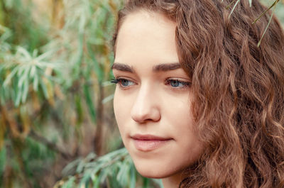 Portrait of girl with brown curly hair on background of green bush sea buckthorn, close-up face