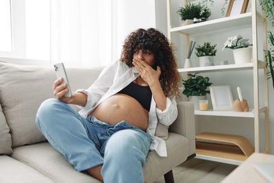 Young woman using mobile phone while sitting on sofa at home