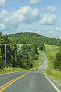 Empty road amidst trees against sky