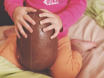 Low section of girl holding easter egg white sitting on bed at home