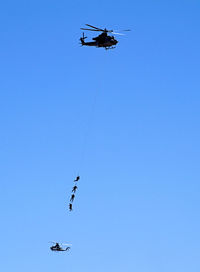 Low angle view of military performing stunts while hanging from helicopter against sky