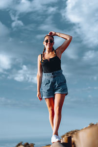 Young woman wearing sunglasses standing against sky