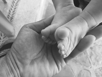 Cropped hand of man holding newborn child feet at home