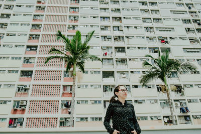 Portrait of woman wearing eyeglasses while standing against building during sunny day