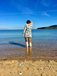 Rear view of boy standing on beach against sky