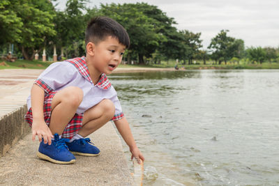Cute boy wearing school uniform crouching by lake
