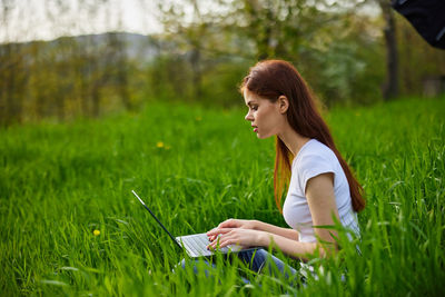 Young woman using laptop while sitting on field