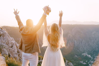 Rear view of friends standing on mountain against sky