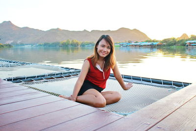 Portrait of smiling woman sitting on net by lake