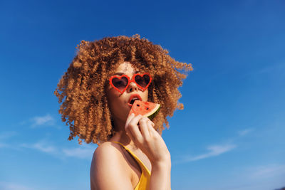 Low angle view of young woman wearing sunglasses against blue sky