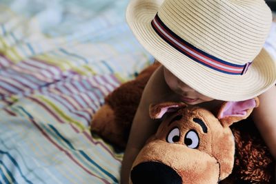 Boy wearing hat holding stuffed toy on bed at home