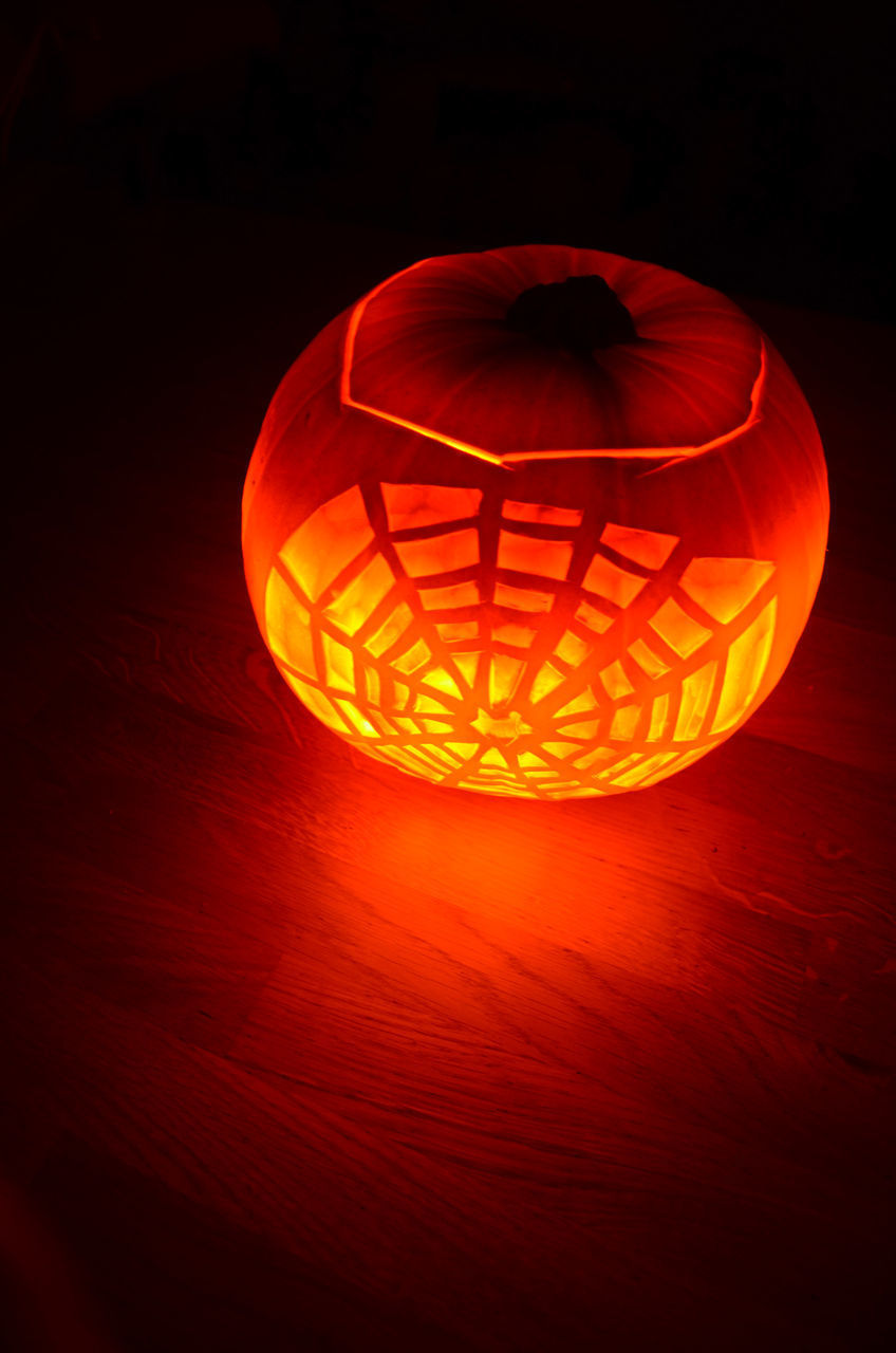 CLOSE-UP OF ILLUMINATED LANTERN ON TABLE AGAINST ORANGE WALL