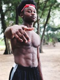 Portrait of shirtless young man gesturing while standing outdoors