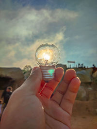Close-up of hand holding crystal ball against sky
