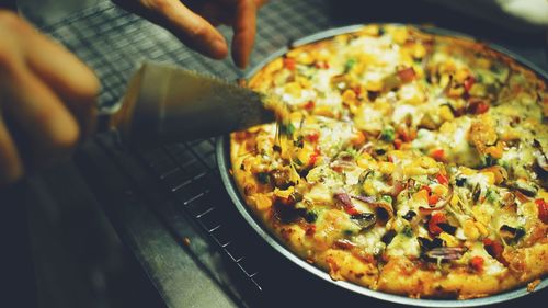 Cropped hands cutting pizza at cooling rack