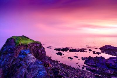 Rocks by sea against romantic sky at sunset