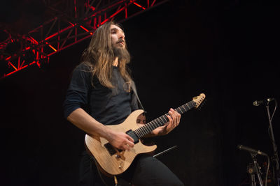 Young woman playing guitar against black background