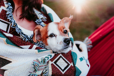 Young woman relaxing with her dog in orange hammock. covering with blanket. camping outdoors. autumn