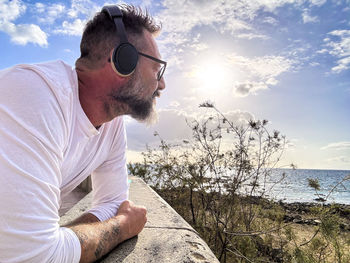 Low angle view of young man wearing sunglasses against sea against sky during sunset