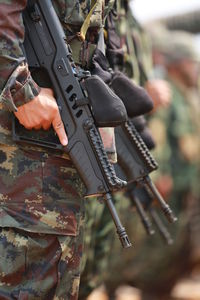 Midsection of army soldiers holding rifles while standing outdoors