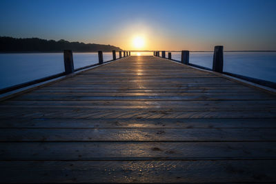 Surface level of wooden pier over sea against sunset sky