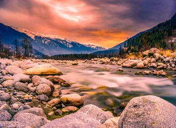 Scenic view of flowing river by mountains against sky during sunset