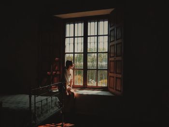 Thoughtful young woman looking through window while sitting at home