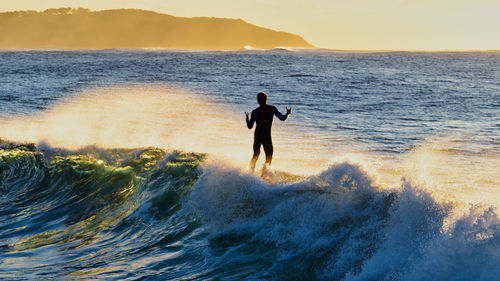 Silhouette man surfing in sea against sky during sunset