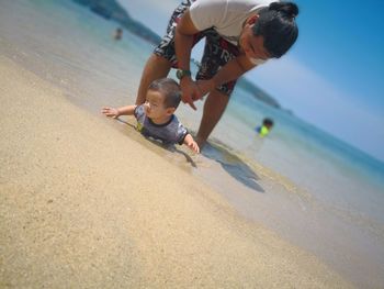 Father looking at son lying on shore at beach during summer