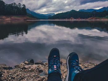 Low section of person by lake against sky