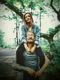Smiling father carrying daughter on shoulders in forest
