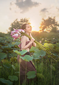Woman standing by flowering plants on field against sky