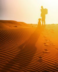 Silhouette man with dog standing on desert against sky during sunset