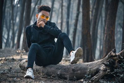 Young man sitting on tree trunk in forest