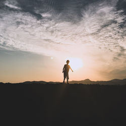 Silhouette boy standing on field against sky during sunset