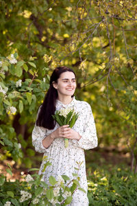 Portrait of young woman standing against trees