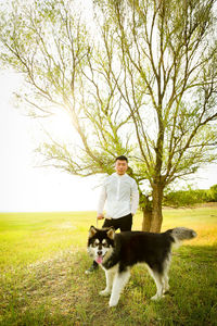 Portrait of man with dog standing on field by tree