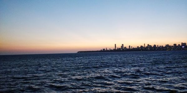 Silhouette buildings by sea against sky during sunset