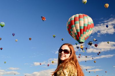Low angle view of woman against hot air balloons against blue sky