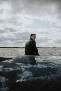 Rear view of man sitting at sea against sky