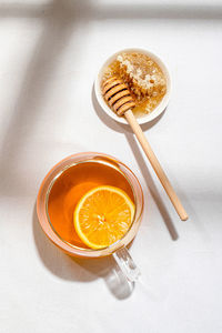 A mug of tea with lemon and a plate of honey on a table covered with a white tablecloth